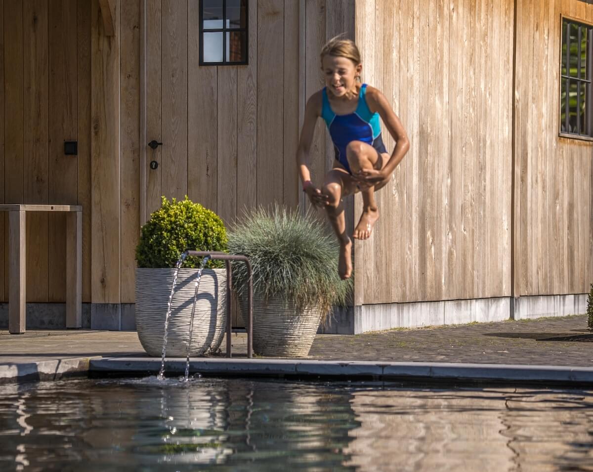 Kind springt in zwembad met op de achtergrond een eikenhouten bijgebouw