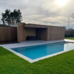 Een modern luxe tuinhuis met overkapping. Vooraan een zwembad.