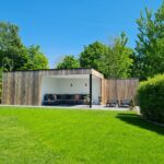 Moderne houten tuinberging met terrasoverkapping.