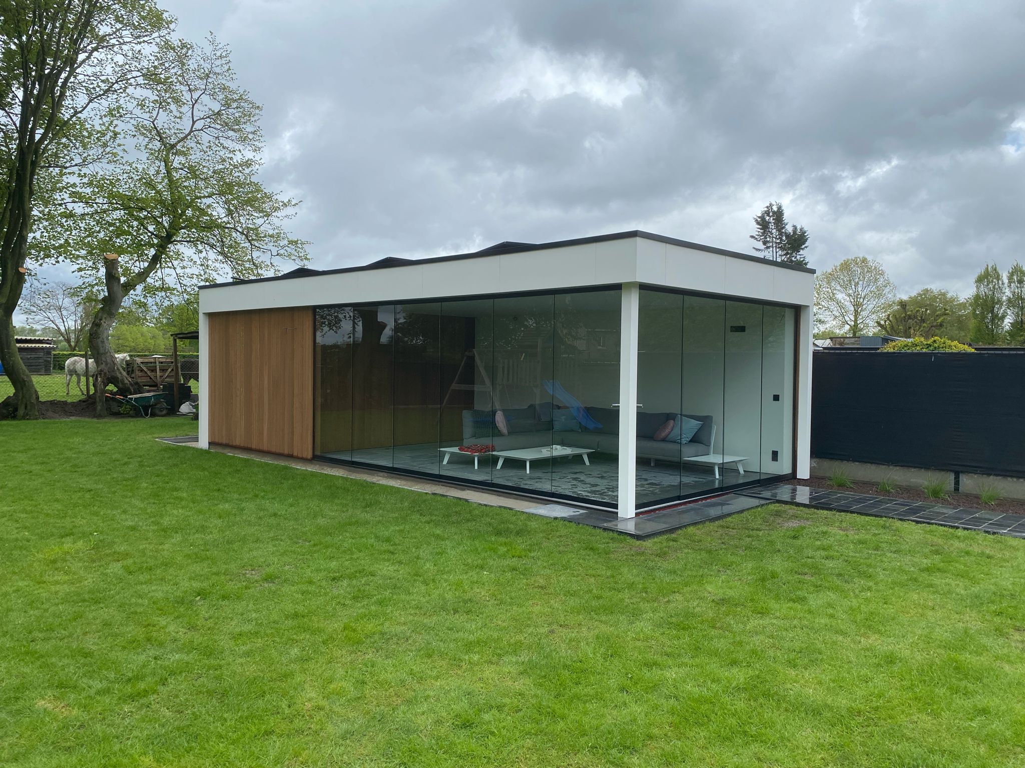 Wit modern bijgebouw met glazen gevels en houten tuinberging.